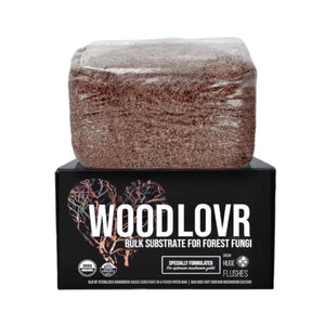 A block of brown, organic hardwood mushroom substrate in a clear filter bag, resting on its branded black display box.