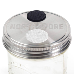 Stainless steel mason jar lid with North Spore logo, a black filter patch, and a white injection port.