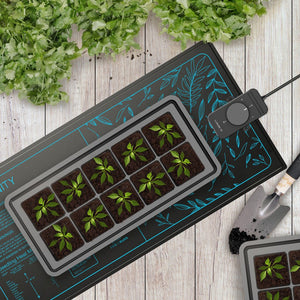 Black seedling heat mat with blue leaf patterns, controller, and 10-cell starter tray with sprouts on wood table.