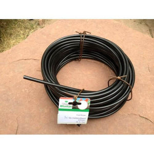 Coiled black irrigation tubing secured with ties, featuring a Tropf Blumat product tag on a flat stone surface.