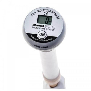 Close-up of a Blumat digital soil moisture sensor with a circular LCD display, ON button, and gray probe handle.