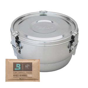 Round stainless steel CVault storage container with locking latches next to a Boveda 62% humidity control packet.
